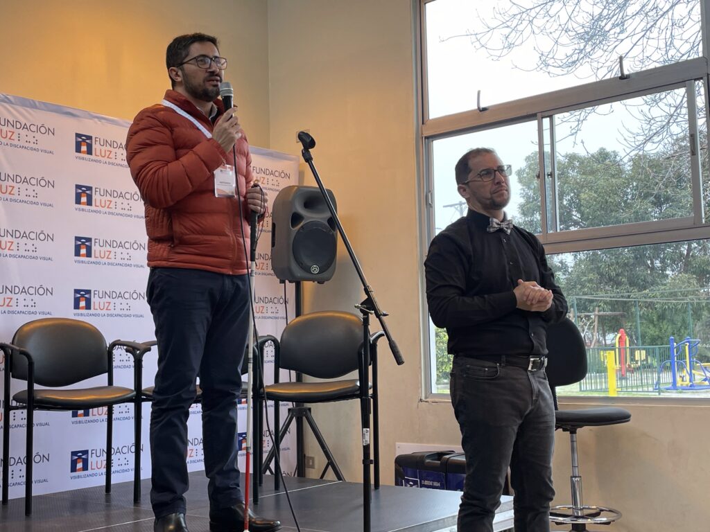 Rubén Carvacho dando su testimonio para Fundación Luz, de pie y con un hombre al lado también de pie
