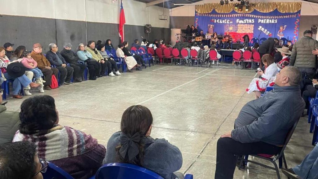 Imagen con el gimnasio decorado y el público asistente, al fondo de divisa la banda.