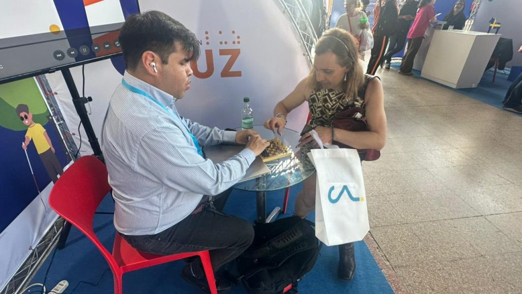 William Cepeda, de Fundación Luz con discapacidad visual, jugando ajedrez con una mujer visitante del stand