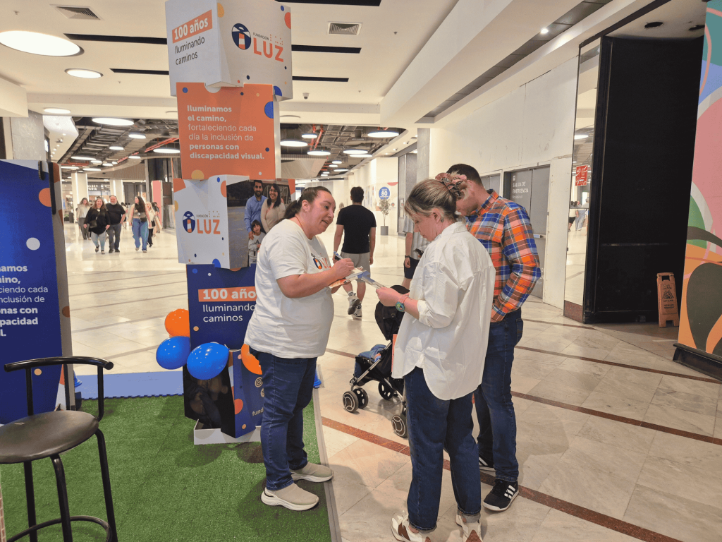 Trabajadora de Fundación Luz entregando información a una pareja que visita el stand.