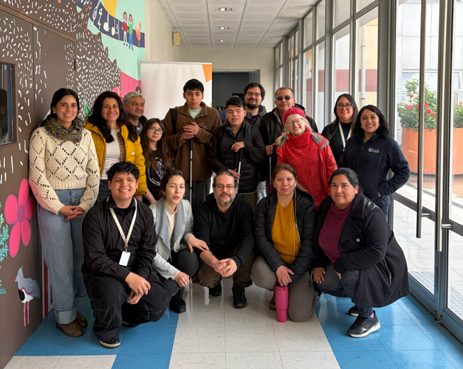 Equipo profesional de Fundación Luz y Demre posan sonrientes junto a los asistentes al ensayo paes. La mayoría está de pie y algunos en cuclillas, en un pasillo del Centro.